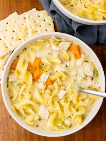 chicken noodle soup in a bowl with crackers on the side